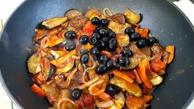 炒菜：洋葱，胡萝卜，辣椒，用黑色橄榄装饰.. 蔬菜炖锅里。 炖菜的过程